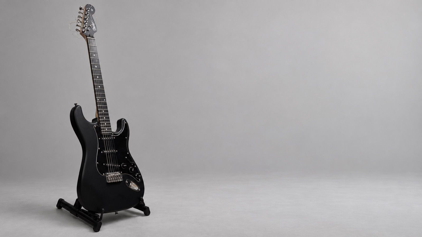 Чёрный Stratocaster на стойке в светло-серой студии